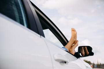 Woman sitting on passenger seat in car with barefoot feet, outside through an open window.