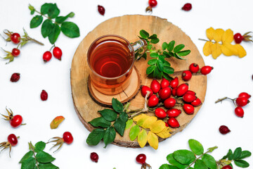 healthy rosehip tea in a glass Cup on a wooden saw, next to dry and fresh rosehip berries on a white surface