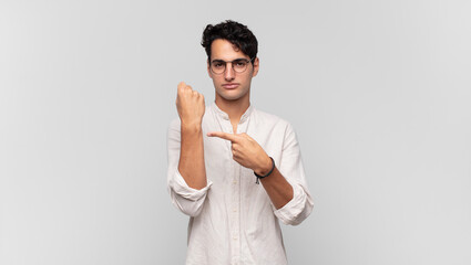 young handsome man looking impatient and angry, pointing at watch, asking for punctuality, wants to...