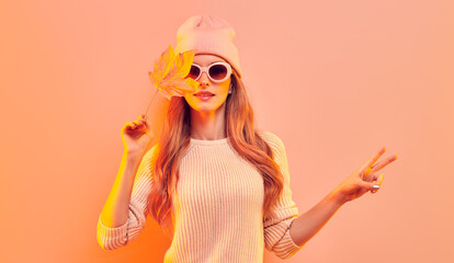 Fashionable hipster woman in Trendy autumn fall outfit, stylish hair, makeup. Blonde model in jumper, fashion jeans having fun smiling. Beautiful girl in autumnal beanie hat with maple leaf