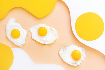 Fried eggs on a light white and yellow wavy background. Paper art. Breakfast concept, fried food.
