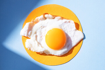 Fried eggs on a light orange and blue background, pattern. Breakfast concept, fried food. Minimalism, top view.