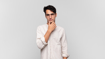 young handsome man looking serious, confused, uncertain and thoughtful, doubting among options or...