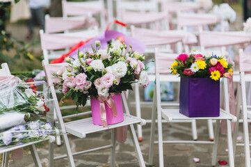 Two paper baskets with yellow, white, red and purple flowers stand on decorated wooden chairs for a wedding ceremony. Photography, concept.