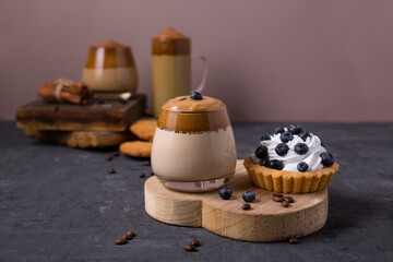 Korean coffee Dalgona Original colors, colored milk with whipped foam in glass glasses on a dark background. Cookies, chocolate, cake. Composition with coffee drinks