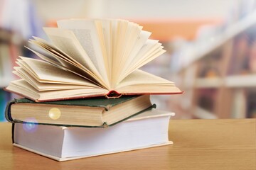 Open book on stack of books with library background.