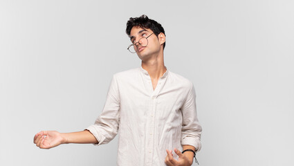 young handsome man shrugging with a dumb, crazy, confused, puzzled expression, feeling annoyed and...