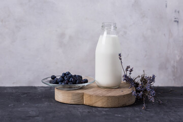 Kumis in a glass bottle on a gray background, lavender and blueberry flowers. Milk drink on a dark...