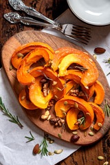 Pieces of sweet spicy pumpkin with nuts on a wooden cutting board close-up. Baked pumpkin with honey, nuts and rosemary. Thanksgiving food. Autumn and winter food.