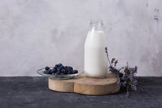 Kumis in a glass bottle on a gray background, lavender and blueberry flowers. Milk drink on a dark background. Place for text