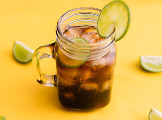 Glass of cola with slice of lemon in mason jar on bright yellow background. Top view composition slices of lemons