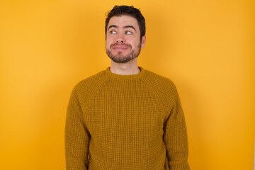 Young man wearing casual sweater and over isolated yellow background looking aside into empty space thoughtful