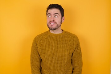 Amazed Young man wearing casual sweater and over isolated yellow background bitting lip and looking up to empty space,