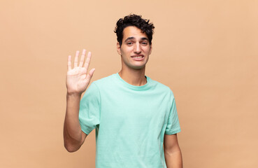 young handsome man smiling happily and cheerfully, waving hand, welcoming and greeting you, or...