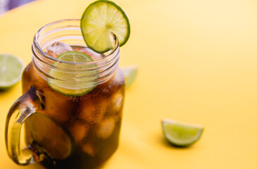 Cola in glass with ice cubes and slices of lemon on bright yellow background