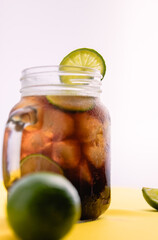 Close up glass of cola with ice cubes and slices of lemon in mason jar on white background
