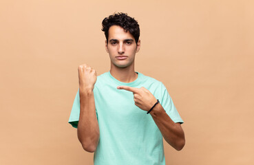 young handsome man looking impatient and angry, pointing at watch, asking for punctuality, wants to...