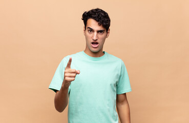 young handsome man pointing at camera with an angry aggressive expression looking like a furious,...