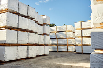 Wooden racks in white packaging film with goods stacked on top of each other in the open air.