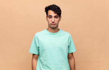 young handsome man feeling sad and whiney with an unhappy look, crying with a negative and...