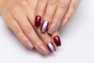 Gel manicure. Beige and burgundy manicure with a wide silver strip on long square nails close-up on a white background.