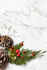 Christmas image/background.Pinophyta, brown pinecone with tree leaves and red fruits on white marble.