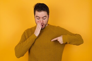 Shocked Young man wearing casual sweater and over isolated yellow background look surprisedly down,...