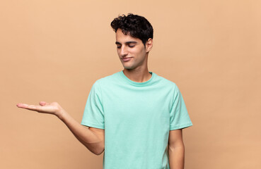 young handsome man feeling happy and smiling casually, looking to an object or concept held on the...