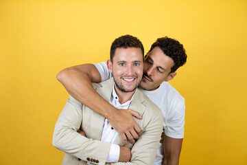 Young gay couple of two men wearing casual clothes over isolated yellow background Standing with smile on face hugging