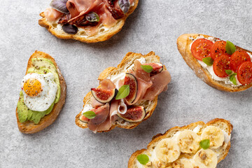 Assorted appetizers, croissant, bruschetta, egg, ham, figs, curd cheese on a gray background