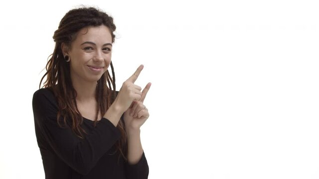 Cute young woman with dreadlocks and ear tunnels, wearing black blouse, pointing fingers at upper right corner, showing logo and smiling, recommending to click link