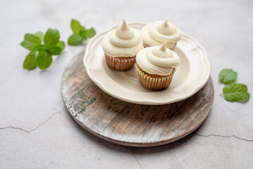 Mini muffins in paper cupcake holder on the wooden tray with white cream cheese frosting