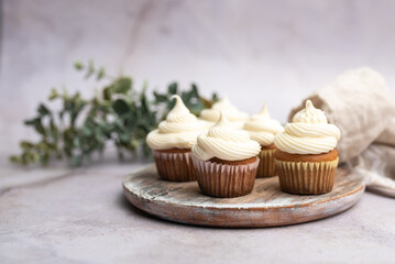 Mini muffins in paper cupcake holder on the wooden tray with white cream cheese frosting