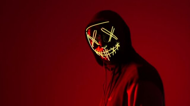 Halloween party. A man in white mask illuminated by neon light close up. Concept of an unknown person and fear