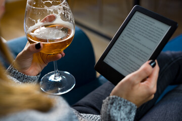 A woman reads from her e-book while enjoying a glass of beer on a couch