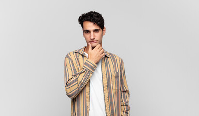 young handsome man looking serious, confused, uncertain and thoughtful, doubting among options or...