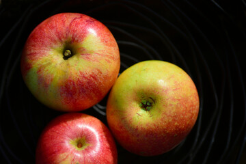 Three apples lie in a black fruit bowl made from a spiral made of iron