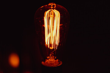 Filament lamp lit with black background, emitting light and brightening the environment