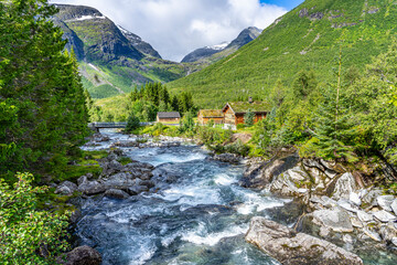 Fototapeta na wymiar Urlaub in Süd-Norwegen: Die schöne idyllische Landschaft mit Bergbach und Holzhütten in der Nähe von Trollstigen