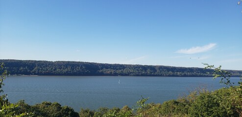 Hudson River viewed at a distance off a vista in Northern Manhattan's Inwood Hill Park. On the river can be seen a sail boat, small at this distance.
