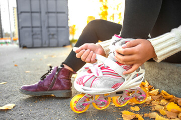 A girl puts on roller skates sitting on a concrete curb. Child fastens roller skates. Close up...