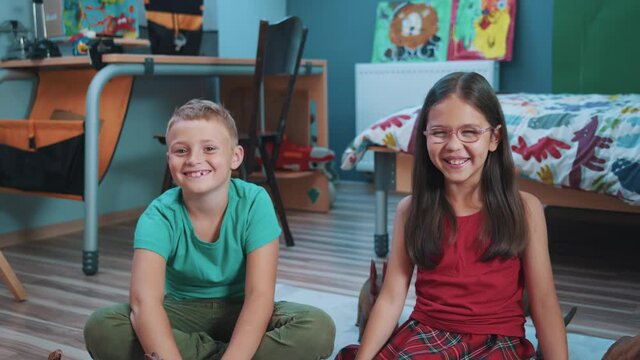 Portrait of cute little brother and sister sitting on the floor laughing excitedly staying home playing. Kids in playroom. Siblings. Lovely family. Childhood concept.