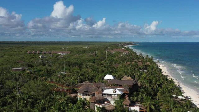 Vista a&eacute;rea sobre la zona de hoteles boutique en Tulum Beach, Quintana Roo, M&eacute;xico.  El drone volando hacia el frente con un cielo azul como fondo.