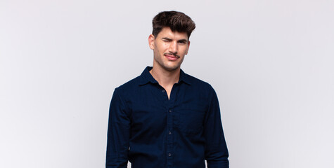 young handsome man looking happy and friendly, smiling and winking an eye at you with a positive...