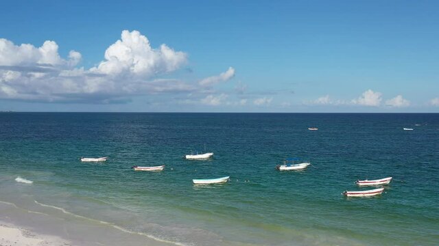 Un grupo de barcas de pescadores atracadas frente a la playa de Tulum, M&eacute;xico con un cielo azul y con pocas nubes como fondo.
