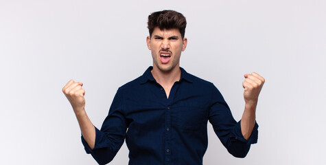 young handsome man shouting aggressively with an angry expression or with fists clenched...