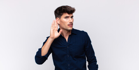young handsome man looking serious and curious, listening, trying to hear a secret conversation or...
