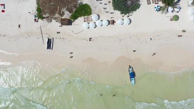 Vista aérea cenital de las olas rompiendo en una playa, con algunas sombrillas y una barca, en el mar caribe.