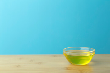 Oil in a glass bowl on a clean blue background. Cosmetic or food oil background. Copy space