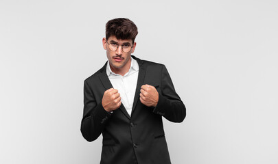young handsome man looking confident, angry, strong and aggressive, with fists ready to fight in...